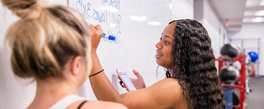 Student writing on whiteboard while another student looks on.